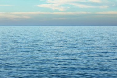 Yumuşak dalgalanmalar ve uzak bir ufka uzanan yumuşak pastel renkler içeren sakin deniz manzarası..