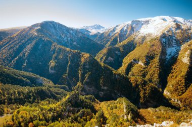 Kafkas dağlarının karla kaplı zirveleri ve renkli sonbahar ormanlarıyla panoramik manzarası.