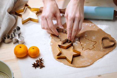 Person uses festive cutters to shape cookies from rolled-out dough, preparing for holiday baking.