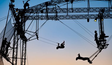 silhouettes of trapeze artists acrobats on the metal scaffolding at sunset