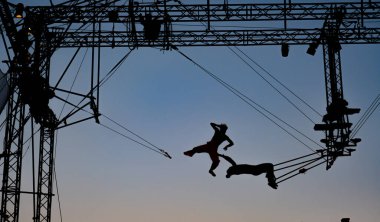 silhouettes of trapeze artists acrobats on the metal scaffolding at sunset
