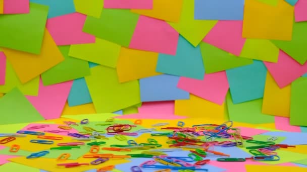 Veelkleurige Paperclips Vallen Langzaam Een Draaiende Tafel Met Veelkleurig Papier — Stockvideo