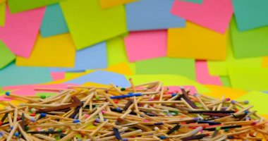 matchsticks of various shapes and colors on a rotating table with multicolored paper sticky notes on background