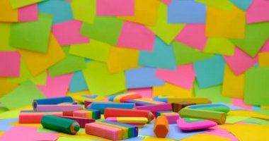 various shapes and colors of erasers arranged on a rotating table with multicolored paper sticky notes on background