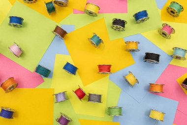 metal spools with Multicolored thread for sewing machine on a  table with multicolored paper sticky notes on background