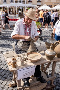 Sibiu City, Romanya - 03 Eylül 2023. Romanya 'nın Sibiu kentindeki çömlekçi fuarında çömlekçi çarkının üzerinde kil çömlek şekillendiren yaşlı bir çömlekçi.