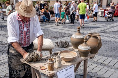 Sibiu City, Romanya - 03 Eylül 2023. Romanya 'nın Sibiu kentindeki çömlekçi fuarında çömlekçi çarkının üzerinde kil çömlek şekillendiren yaşlı bir çömlekçi.