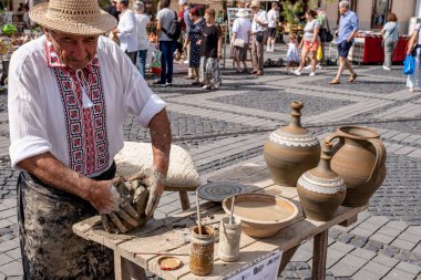 Sibiu City, Romanya - 03 Eylül 2023. Romanya 'nın Sibiu kentindeki çömlekçi fuarında çömlekçi çarkının üzerinde kil çömlek şekillendiren yaşlı bir çömlekçi.