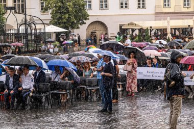 Sibiu City, Romanya - 11 Haziran 2024. Şiddetli bir yağmurun altında öğrencilerin şapkalarını havaya attıkları mezuniyet töreni.