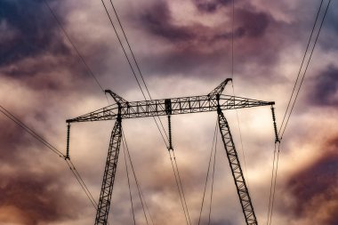 Transformer Substation 'da seramik yalıtımlı yüksek voltajlı elektrik şebeke kutuplarının silüeti ve kara bulutlarda Corona boşalması.