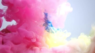 Pink and blue colored ink burst in water and form an abstract smoke pattern