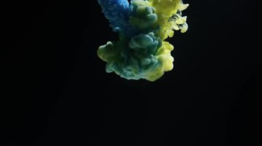 Blue and yellow colored ink burst in water and form an abstract smoke pattern