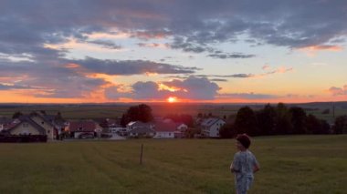 Little brother and sister having fun running through grass field towards residential town during sunset