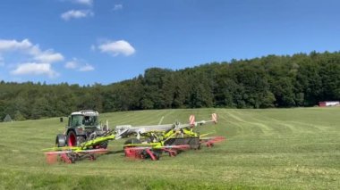 Tractor raking grass crop into rows for baling