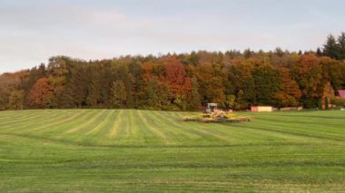 Tractor raking grass crop into rows for baling