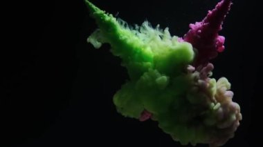 Pink and green colored ink burst in water and form an abstract smoke pattern