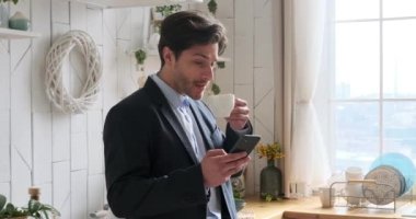 Kahve içen ve mesajlaşan bir iş adamı mutfaktaki cep telefonunu kullanıyor.