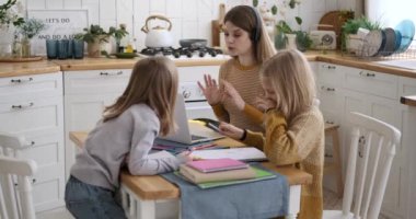 Beyaz iş kadını dizüstü bilgisayarla video görüşmelerini tartışırken evde oturup ödev yazan kızlarıyla birlikte.