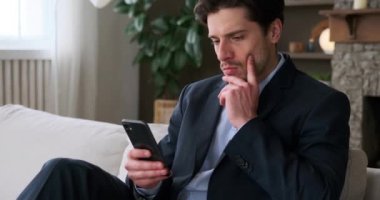 Ciddi bir iş adamı koltukta oturuyor ve cep telefonuyla mesaj okuyor.