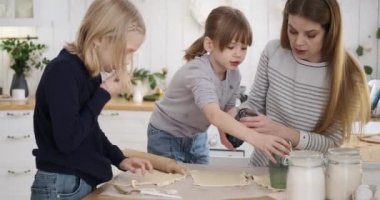 Genç anne, evde mutfak masasındaki kurabiyeler için cam ve çatalla hamur kesmeyi öğretiyor.