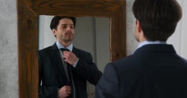 Yakışıklı iş adamı kravatını düzeltip aynanın önünde ceketini ilikleyerek hazırlanıyor.