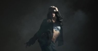 Smoky stüdyo arka planında hip hop serbest dans eden şık genç bir kadın.