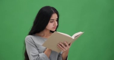 Düşünceli genç kadın yeşil ekranda kitap okuyor.