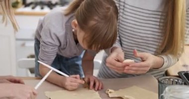 Beyaz tenli genç anne konuşuyor ve tatlı kızlarına hafta sonu mutfakta taze kurabiye hazırlamada rehberlik ediyor.