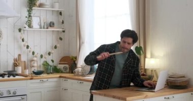 Adam mutfakta dizüstü bilgisayar kullanırken dans edip şarkı söylüyor.