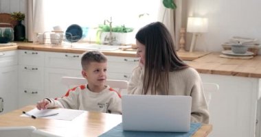 Gülümseyen anne dizüstü bilgisayar kullanıyor ve oğluyla konuşuyor.