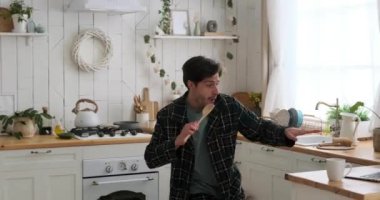 Adam mutfakta dizüstü bilgisayar kullanırken şarkı söyleyerek ve dans ederek eğleniyor.