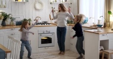 Mutfakta dans ederken elinde spatula tutan ve zıplayan neşeli anne ve kızların yavaş çekim görüntüleri.