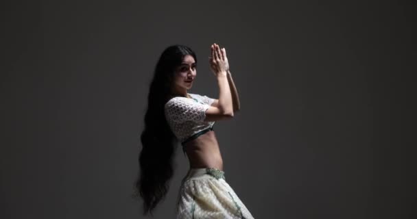 伝統的なサリーのドレスを着た若いインド人女性が 暗いスタジオの背景で美しく表現力豊かなインド舞踊を披露します 彼女の白いサリーは複雑な宝石で飾られています — ストック動画