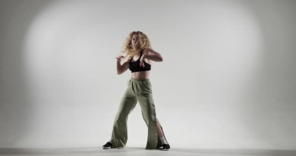 白人妇女在洁白的背景上跳舞 她充满活力的绿色裤子和精力充沛的动作散发着积极向上和热情 她的传染性能量和富有表现力的舞蹈编排 — 图库视频影像