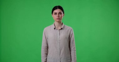 Ciddi görünüşlü bir kadın yeşil ekrana karşı duruyor ve itiraz ve reddedilmeyi ifade etmek için dur işareti olarak avucunu gösteriyor. Günlük kıyafetler giyiyor ve atkuyruğu var..