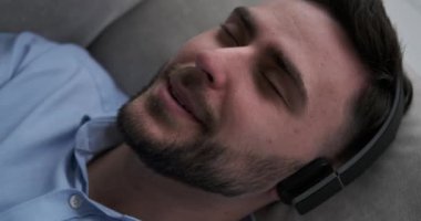 Kafkasyalı bir adam kanepede uzanıyor, kulaklık takıyor ve müzik eşliğinde şarkı söylüyor, hem de kendini tamamen rahat ve rahat hissederken. Huzurlu atmosfer, müziğin rahatlatıcı sesleriyle birleşir.