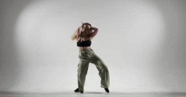 Genç beyaz kadın zarif hareketler ve duygusal performans sergiliyor. Çağdaş dansın özünü hayata geçiriyor. Beyaz arka planda, canlı yeşil pantolon giyiyor..