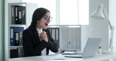 Ofis masasında oturan Hintli iş kadını özenle dizüstü bilgisayarında çalışıyor, harika bir haber alıyor, yüzü coşkuyla 