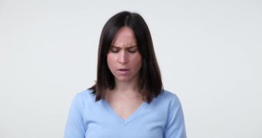 Beyaz bir arka plana karşı duran beyaz bir kadın, elini şakağına koyuyor. Düşünceli bir ruh hali içinde, düşüncelere dalmış ve derin düşüncelere dalmış gibi görünüyor..