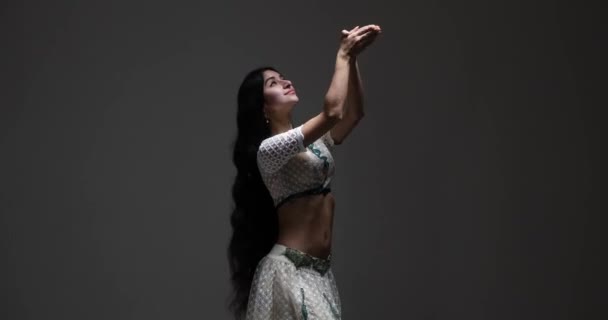 一位身穿白色萨里的年轻印度妇女 戴着迷人的珠宝 在黑暗的背景下表演着迷人的舞蹈 她活泼的动作和富有感染力的微笑会让你保持沉醉 — 图库视频影像