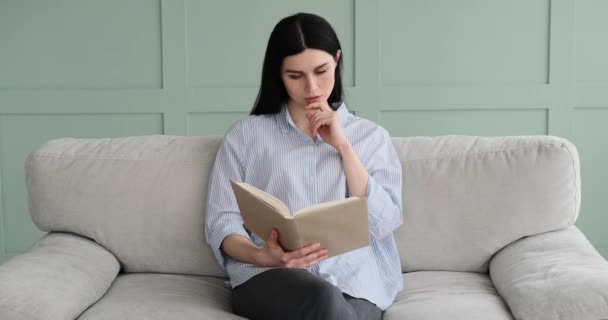 ソファに座って本を読んでいる白人系白人の民族の焦点を当てた白人女性の肖像画 彼女は深い集中力でページをめくる — ストック動画