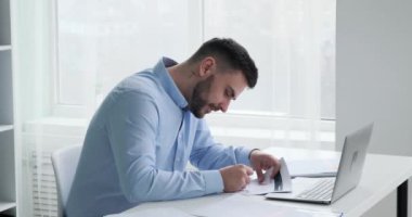 Ofiste sakallı bir iş adamı çalışıyor. Masasında ayrıntılı grafikler ve istatistiklerin yer aldığı belgeleri dikkatle inceliyor. Kalemle not alıyor..