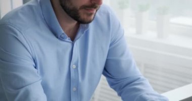 Ofisinde oturan ve dizüstü bilgisayarında yazan beyaz bir iş adamı. Yüzünde sakin bir ifadeyle, kendinden emin ve işine odaklanmış görünüyor..