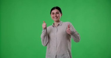 Kafkas kökenli neşeli bir kadın, günlük kıyafetler giymiş, yeşil bir perde arkasında duruyor. Dans eder, güler ve olumlu enerji ve neşe saçan bir jest gösterir..