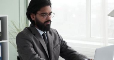 Gözlüklü ve takım elbiseli Hintli bir işadamı pencerenin önündeki bir ofiste oturup dizüstü bilgisayarı üzerinde çalışıyor. Sonra bir problem hakkında derin düşüncelere daldı ve ilham almak için pencereden dışarı baktı..