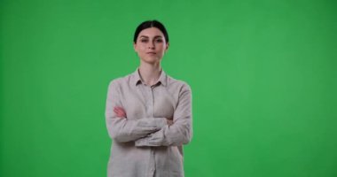 Yeşil ekran arka planında, kendine güvenen beyaz bir kadın kollarını göğsünde kavuşturmuş, doğrudan kameraya bakıyor, özgüven ve güç yayıyor..