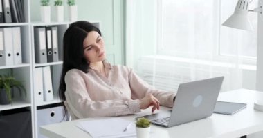 Başarılı bir beyaz kadın girişimci ofisteki bir dizüstü bilgisayarla işini bitiriyor. Dizüstü bilgisayarı kapatıyor, derin bir nefes alıyor ve uzun bir günün gerginliğini atmak için boynuna masaj yapıyor..