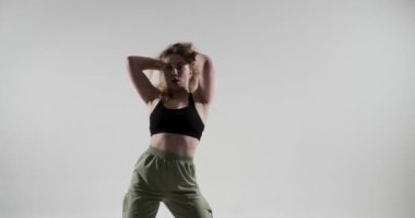 Beyaz arka planda, yeşil pantolon giyen beyaz kadın hip hop dans yeteneklerini sergiliyor. Canlı performansı ve etkileyici hareketleriyle heyecan ve canlılık hissi getiriyor..