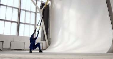 Uzman spor kıyafetli bir kadın barfiks çekerek çömelme hareketleri yapıyor. Egzersiz, izleyicinin kadın tekniğini görmesini sağlayan merkezi bir bakış açısından çekiliyor..