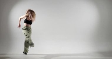 Stüdyoda beyaz bir arkaplana karşı çekilen beyaz kadın, enerjik ve anlamlı dans hareketleri sergiliyor. Göz alıcı yeşil pantolonları, büyüleyici performansı ve bulaşıcı enerjisi vardı..